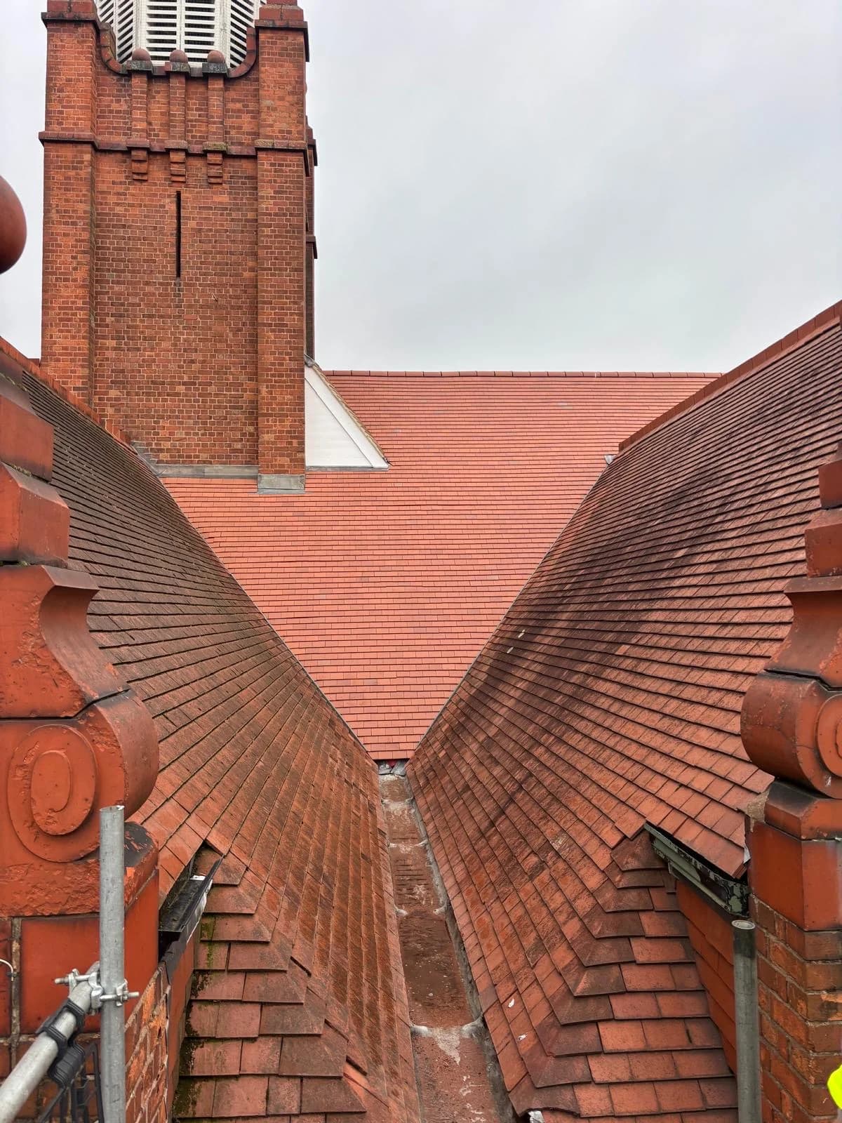 Red clay tiled roof valleys meeting a tall brick chimney