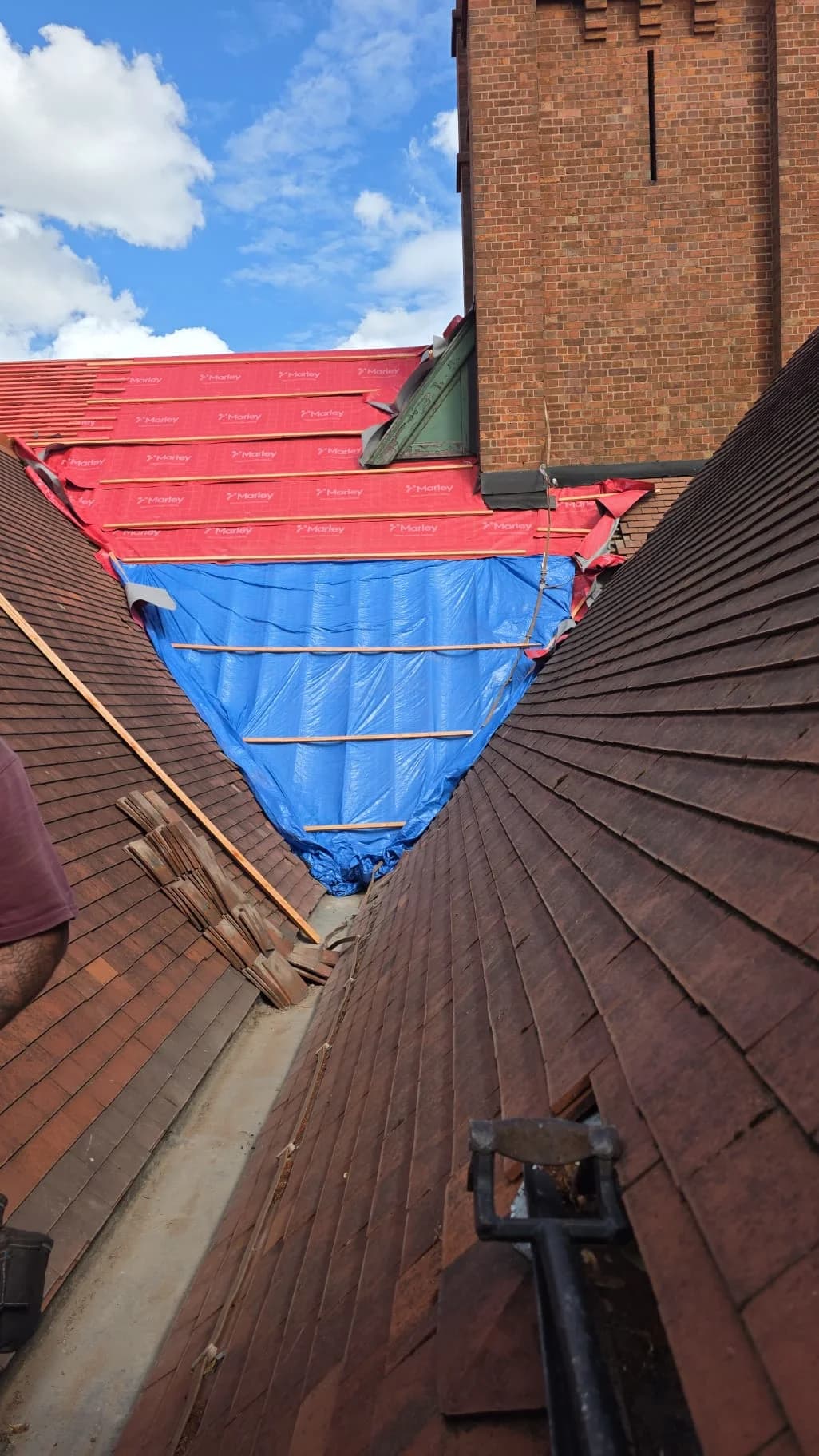 Red tiled roof slope with blue protective sheeting